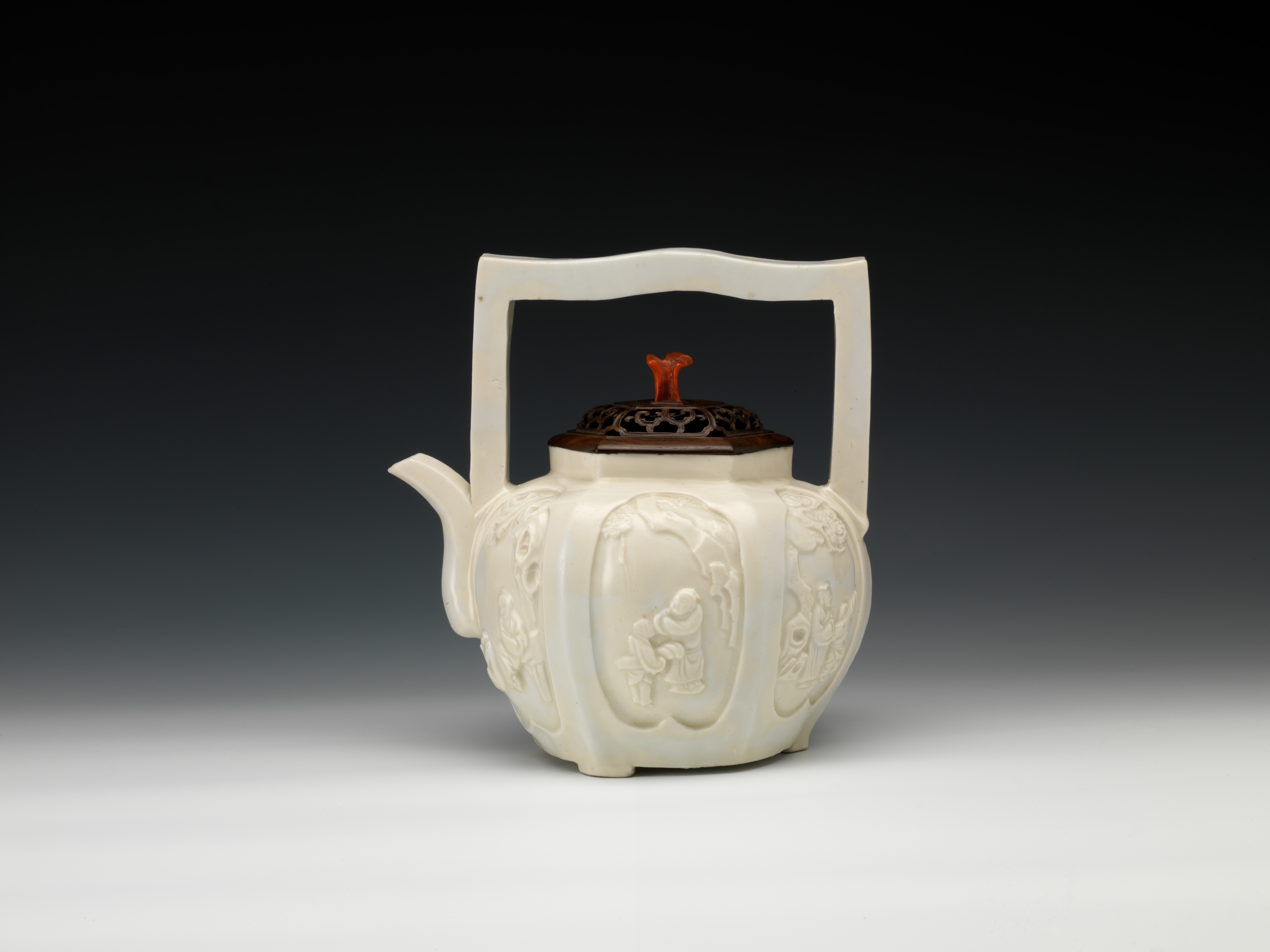 Teapot of six-lobed shape with overhead handle and moulded figure design inside reserved panels in white glaze, Dehua ware